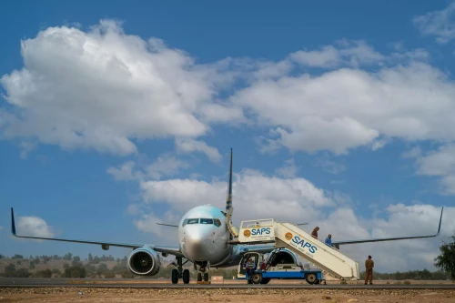 A Boeing 737 is parked on the apron with passengers boarding via a staircase.