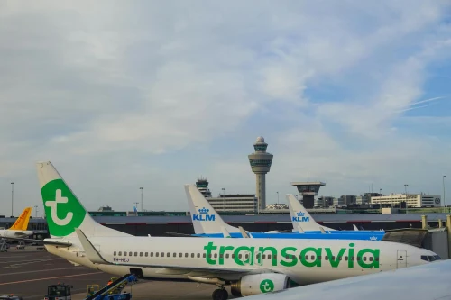 A Transavia Boeing 737 parked at the airport apron with KLM aircraft and control towers in the background.