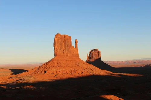 Golden hour illuminates the majestic Mittens rock formations in Monument Valley