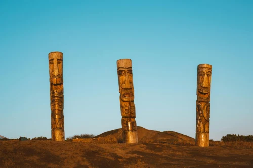 Ancient pagan wooden pillars with faces of people in middle of empty dry plain with blue clear sky on background