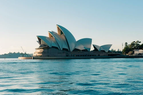 Scenic view of the iconic Sydney Opera House against a clear morning sky with calm water reflections