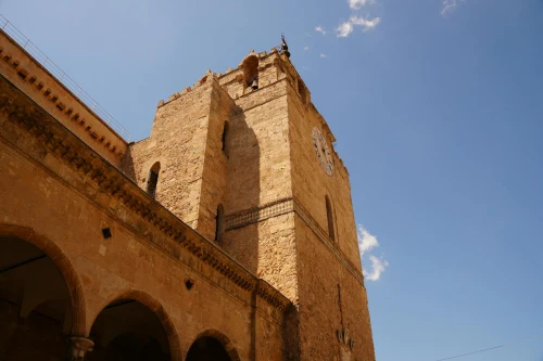 Wide-angle view of Monreale Cathedral's historic bell tower against a vivid blue sky in Sicily, Italy