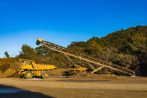 Yellow dump trucks and conveyor machinery in a sunny mining site with clear blue sky