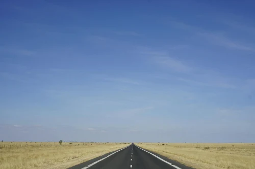 Wide open road stretching through desert landscape beneath a vast blue sky, perfect for travel themes