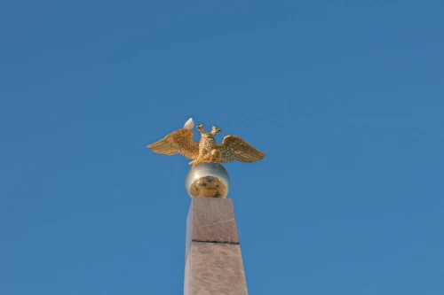 A golden eagle statue perched on a monument with a vivid blue sky background