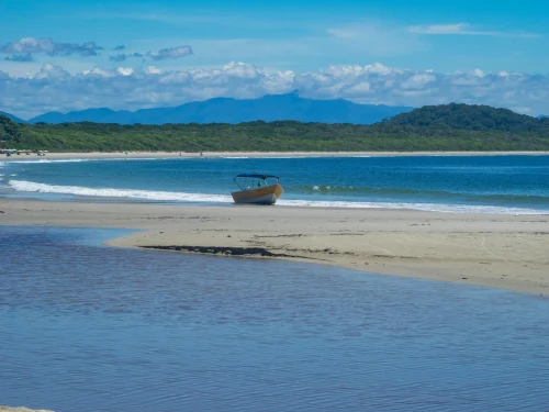 A solitary boat rests on a tranquil beach with lush hills and a vibrant blue sea