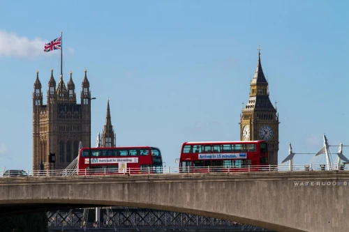 Iconic red double-decker buses crossing Waterloo Bridge with Big Ben and Victoria Tower in the background