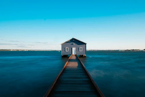 Blue boathouse on ocean with jetty, famous Perth landmark under clear sky