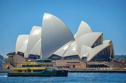 Iconic Sydney Opera House with a passing ferry on a sunny day, showcasing Sydney's vibrant waterfront