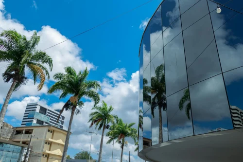 Reflective glass building and palm trees under a vibrant blue sky in Campina Grande, Brazil