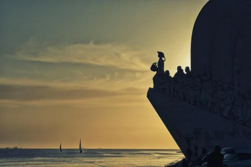 Silhouette of the Discoveries Monument in Lisbon at golden hour with ocean view and sailboats