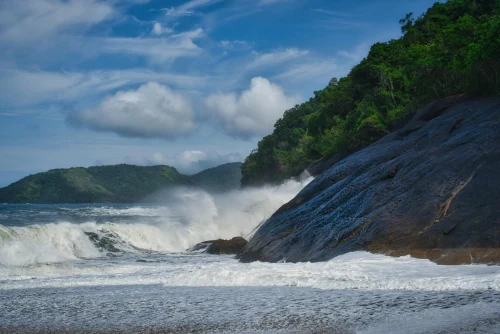 Majestic coastal view of waves crashing against rocky shores in Ubatuba, Brazil, under a clear blue sky