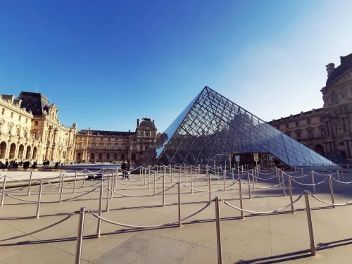 Louvre Pyramid in Paris with bright sky, showcasing iconic architecture and clear reflections