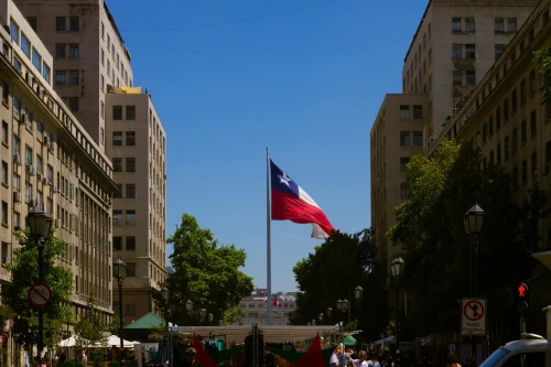 Chilean flag waving between historic buildings in a bustling Santiago city street on a sunny day