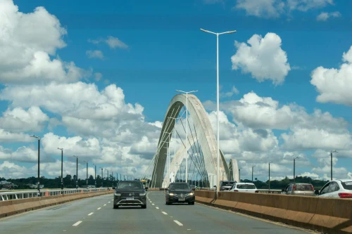 Cars driving on the iconic Juscelino Kubitschek Bridge in Brasília, Brazil against a background of fluffy clouds and blue sky