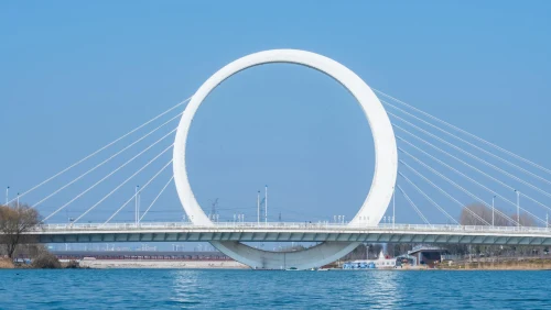 The iconic Infinity Ring Bridge in Zhengzhou, China, spanning over a tranquil river under a clear sky