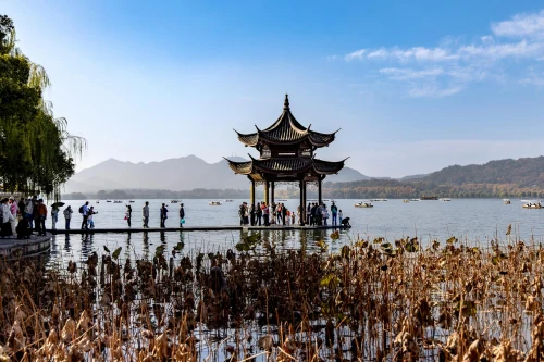 Visitors admire a traditional pagoda on West Lake, surrounded by serene water and mountains in Hangzhou