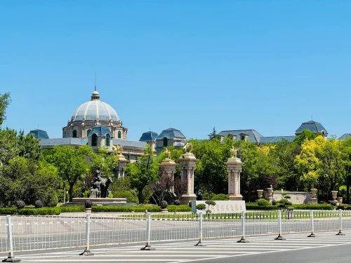 Grand architectural building with a dome, surrounded by greenery and adorned with statues on a sunny day