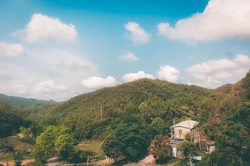 Scenic view of a rural Chinese landscape with a house, hills, and lush greenery under a bright blue sky