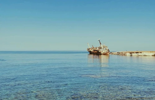 A scenic view of an abandoned shipwreck near the coast of Paphos, Cyprus, under a clear blue sky