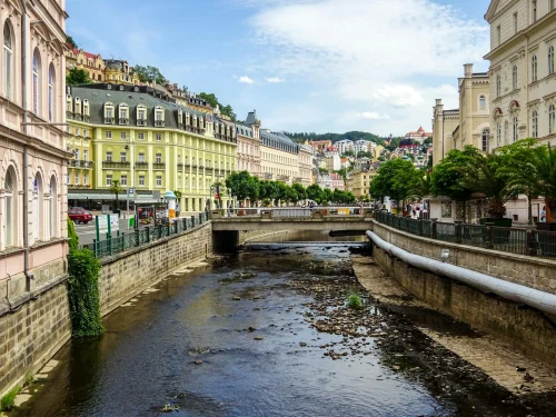 Scenic view of Karlovy Vary's canal with historic buildings and lush greenery under a blue sky