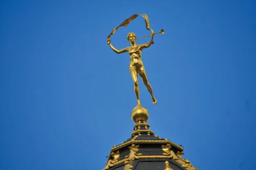 A stunning golden statue stands gracefully atop a building with a clear blue sky backdrop