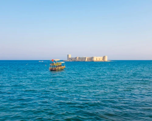 Scenic view of Kizkalesi Castle and a fishing boat on the blue Mediterranean Sea under a clear sky