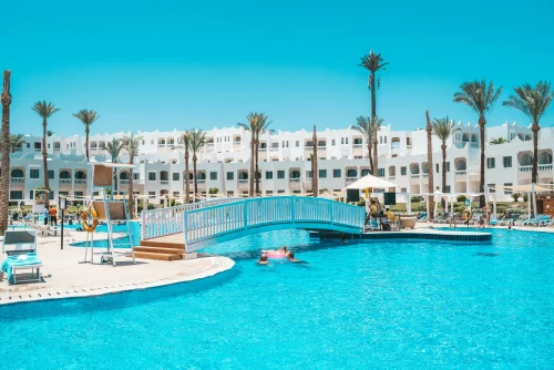 Scenic view of a resort pool with a footbridge and palm trees under a clear sky
