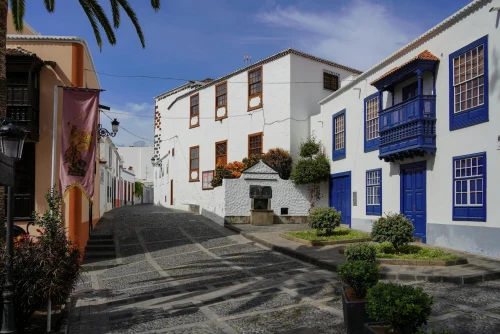 A picturesque cobblestone street in La Palma, Spain, with colorful houses and lush greenery under a bright blue sky