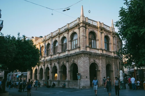Iconic view of Heraklion (HER), greece — A picturesque historic building in a European town square captured at dusk, with people strolling nearby..