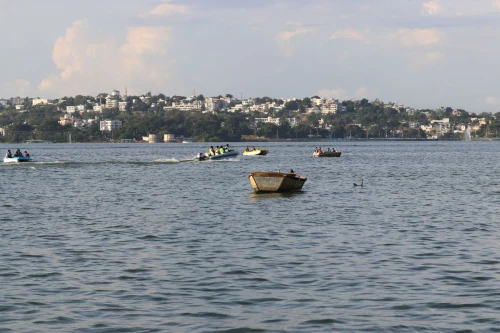 Boats float on Upper Lake in Bhopal with a cityscape in the background under a sunny sky