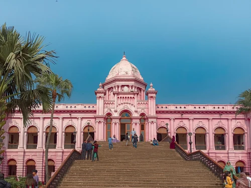 People outside the iconic pink Ahsan Manzil Palace in Dhaka, Bangladesh. Clear blue sky backdrop