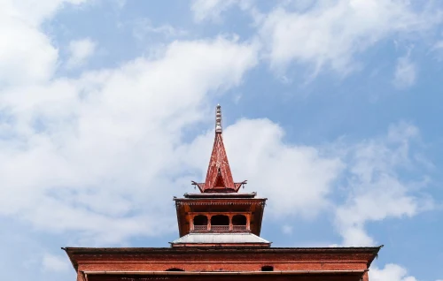 Captivating view of a mosque spire with intricate design, set against a bright blue sky with scattered clouds