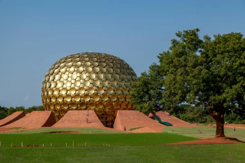 The iconic Matrimandir in Auroville, Puducherry, surrounded by green lawns and a vibrant tree under a clear blue sky