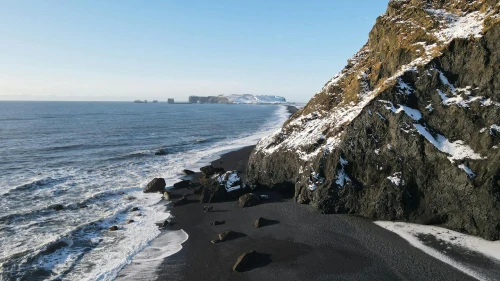 A mesmerizing view of Iceland's black sand coastline with snowy cliffs and ocean waves under a clear blue sky