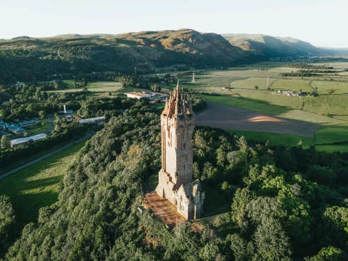 Aerial shot of the historic Wallace Monument surrounded by lush greenery in Scotland, captured at golden hour