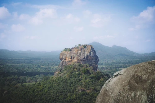 A stunning view of Sigiriya Rock Fortress in Sri Lanka, surrounded by lush greenery under a bright blue sky