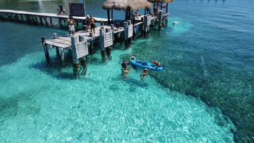 People enjoying a sunny day at Isla Mujeres pier with clear water and vibrant scenery