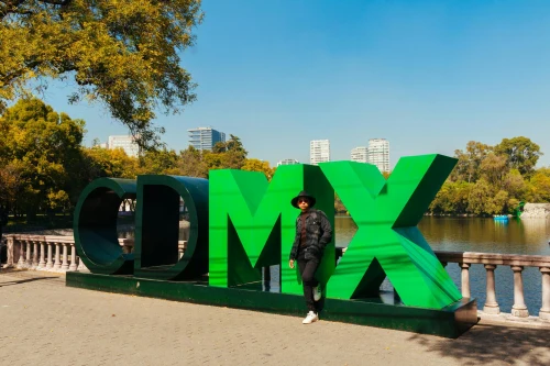 Man standing by the iconic green CDMX sign in a sunny urban park in Mexico City