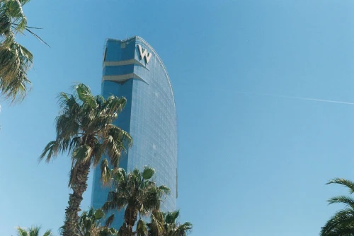 View of the iconic W Barcelona Hotel with palm trees under a clear blue sky in Barcelona, Spain