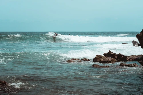 A surfer riding the waves at Puerto Escondido's stunning rocky coastline under a clear sky