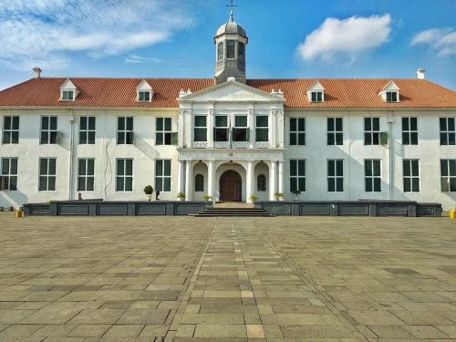 A grand colonial-style white building with a red roof against a blue sky
