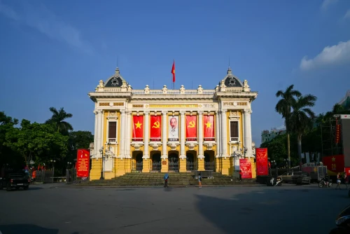 Front view of the historic Hanoi Opera House adorned with red communist banners under a clear blue sky