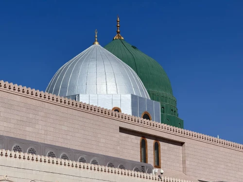 The iconic green and silver domes of Masjid Nabawi under a clear blue sky in Madinah, Saudi Arabia