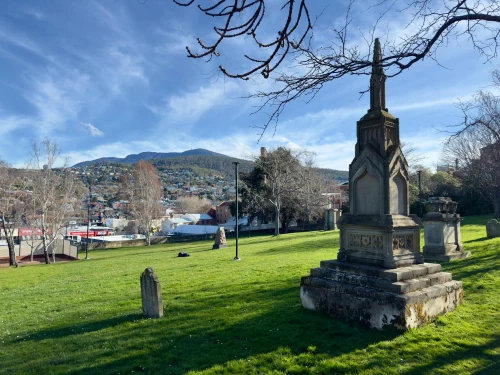 Old cemetery with a historic tombstone in Hobart, Tasmania, under a clear blue sky and mountain backdrop