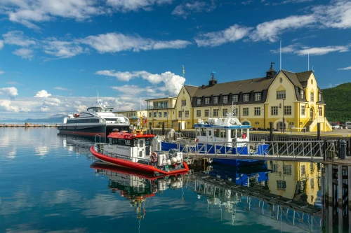 Scenic view of Harstad harbor with vessels moored by the landmark yellow building on a sunny day