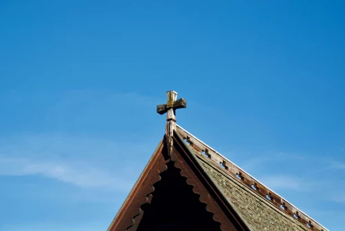 A detailed view of a wooden cross atop a traditional Norwegian church roof against a clear blue sky