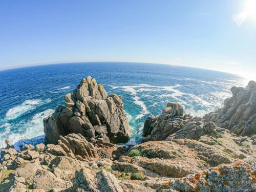 Stunning rocky cliffs meet the ocean waves under a clear blue sky in Cornwall, England