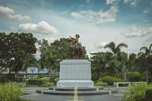 Iconic view of Dipolog (DPL), philippines — A magnificent bronze statue stands in a vibrant park in the Philippines, surrounded by lush greenery and palm trees..