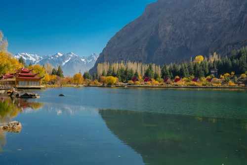 Peaceful autumn scene of a lake and mountains in Skardu, with vibrant foliage and a clear sky